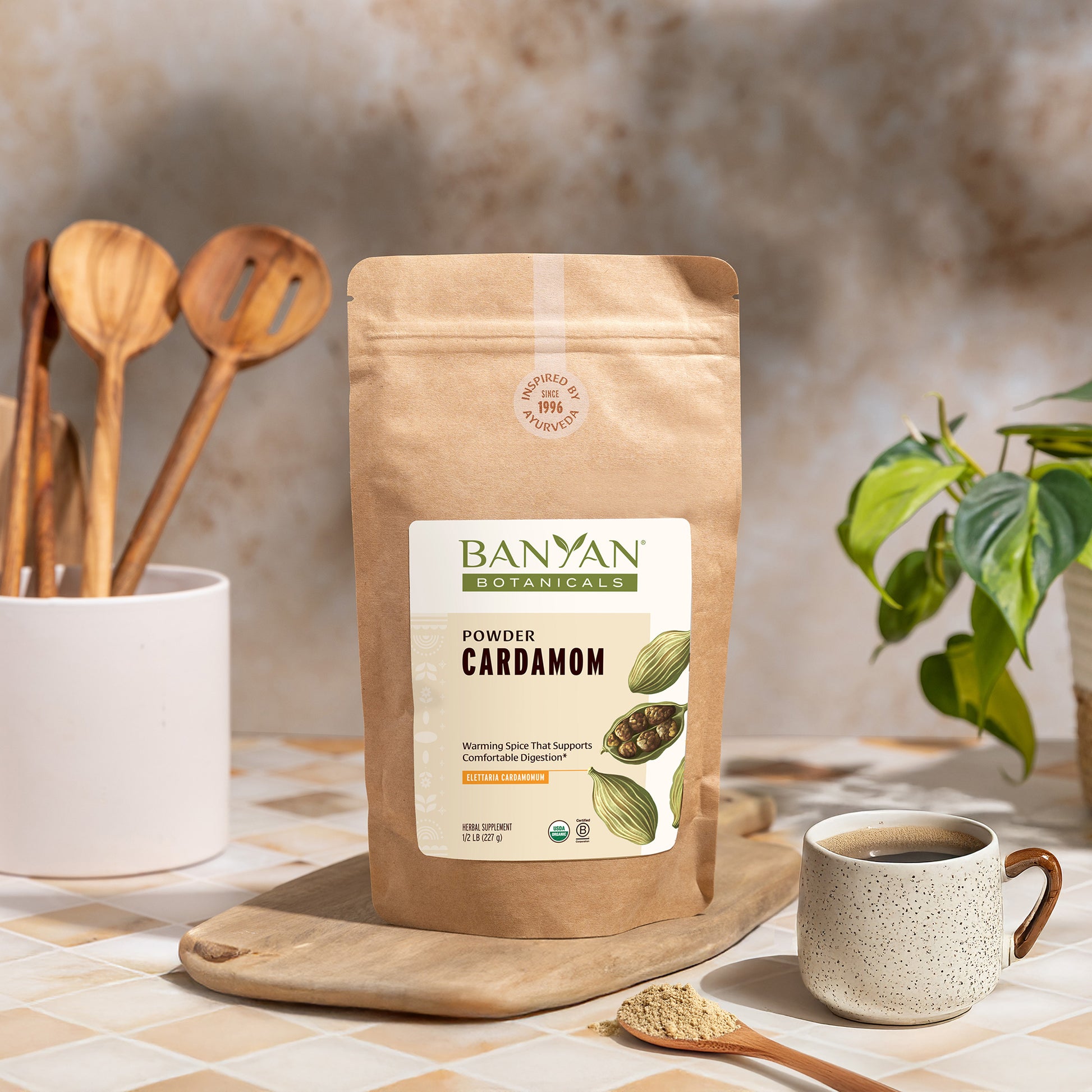 1/2 lb: Cardamom powder pouch on a wooden cutting board with a cup of coffee and spoon.